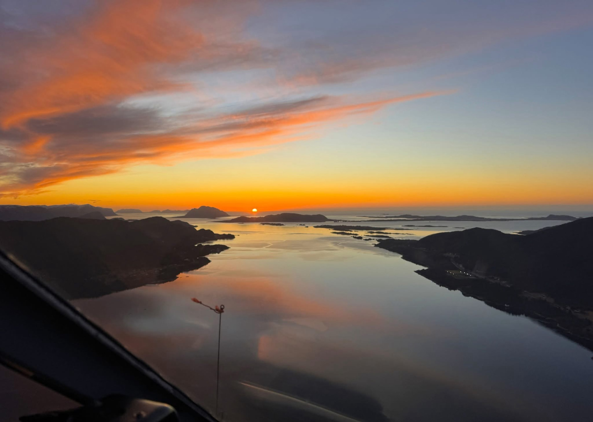 Utsikt fra helikopter med lasteline mot solnedgang over norsk kystlandskap
